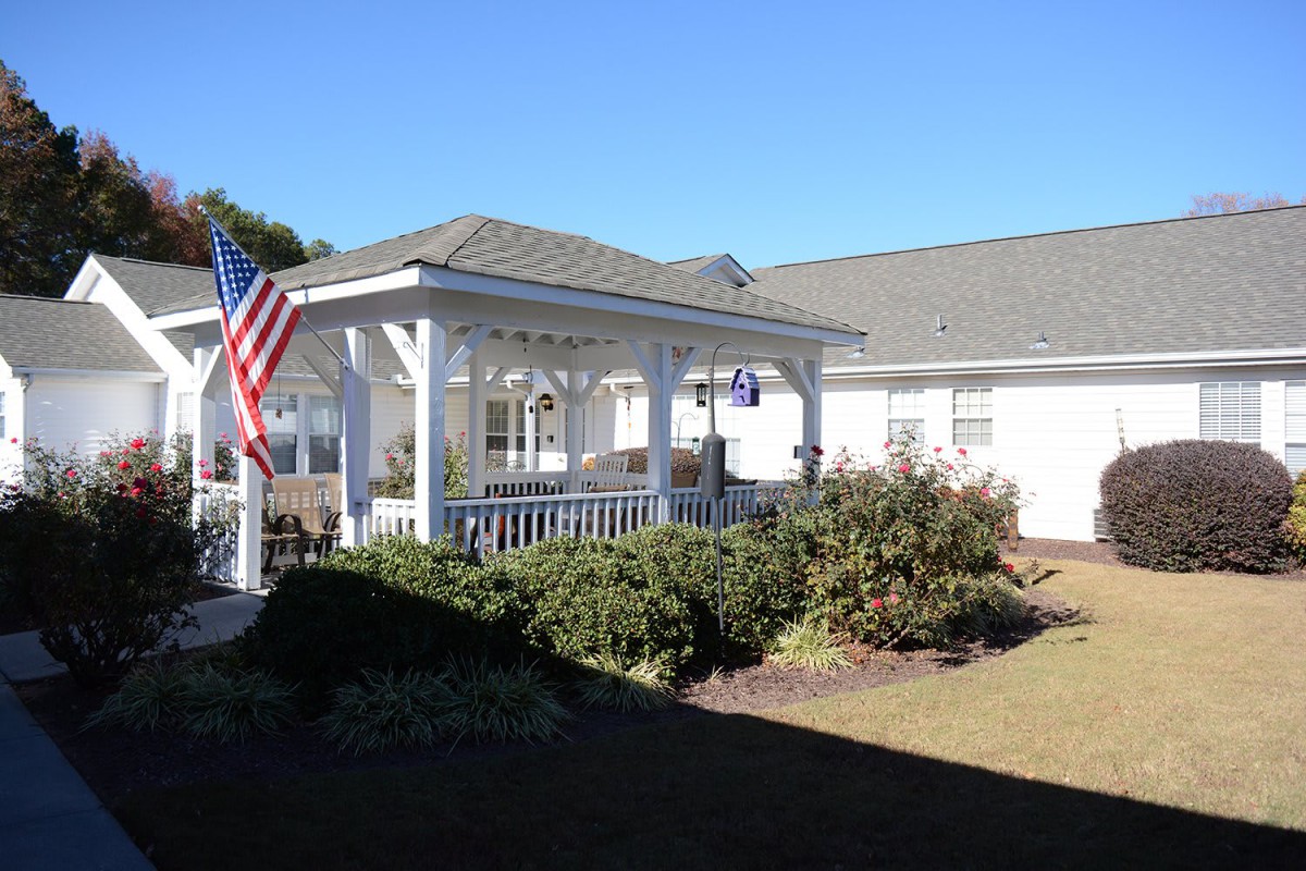 A white building with a covered patio and an American flag, set in a landscaped outdoor area.