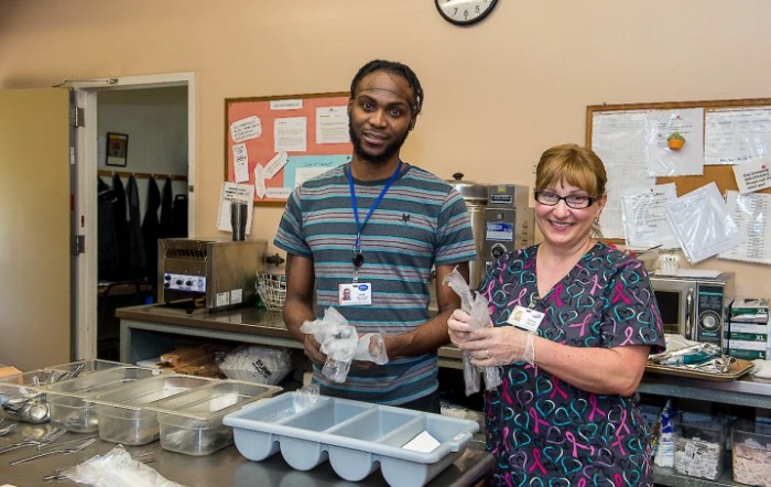 Two people working together in a kitchen, preparing meals and wearing uniforms.