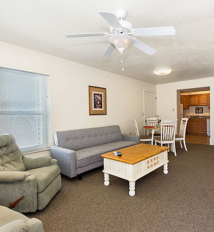 A cozy living room with a sofa, armchair, and coffee table, adjacent to a dining area.