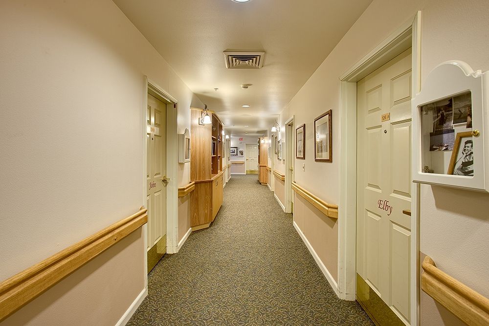 A well-lit hallway with handrails, carpeted floor, and multiple doors on either side.