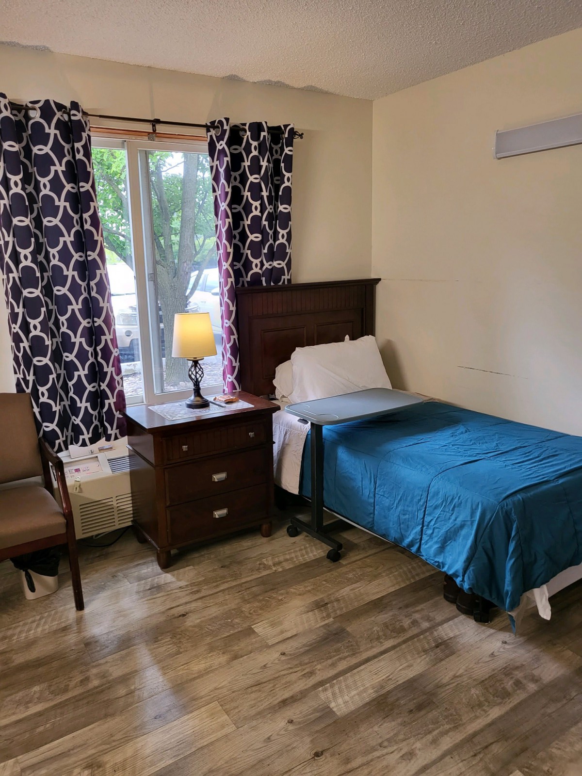 A cozy bedroom with a single bed, nightstand, and a lamp by the window.
