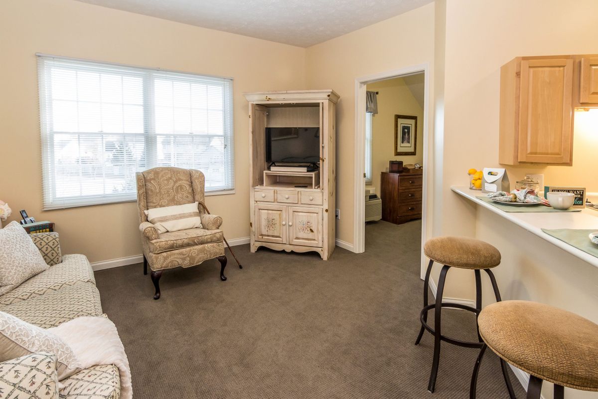 A cozy living room with an armchair, TV stand, and bar stool in neutral colors.