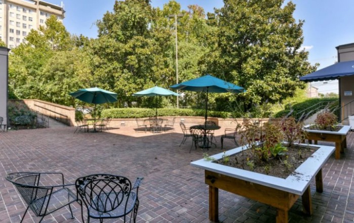 A serene outdoor patio with tables, chairs, and umbrellas surrounded by greenery.