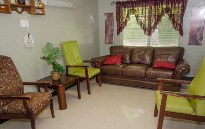 A cozy living room with a brown leather sofa, two green chairs, and a wooden coffee table set against a window with elegant curtains.