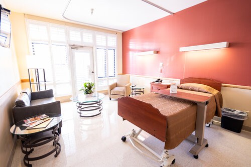 A clean and bright hospital room with a bed, furniture, and large windows.