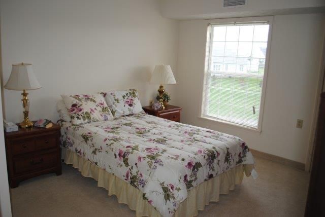 A cozy bedroom with a floral bedspread and a lamp by the window.