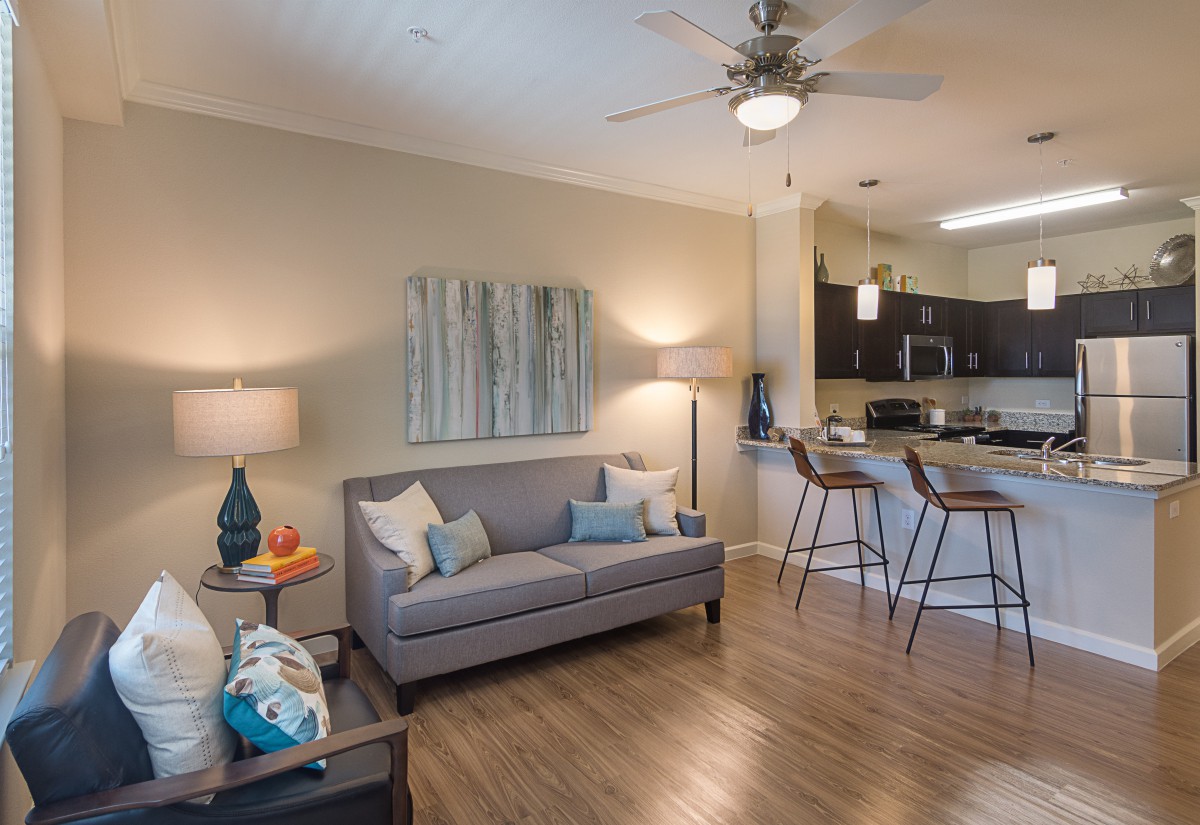 A modern open-concept living room with a view of the kitchen, featuring stylish decor and wood flooring.