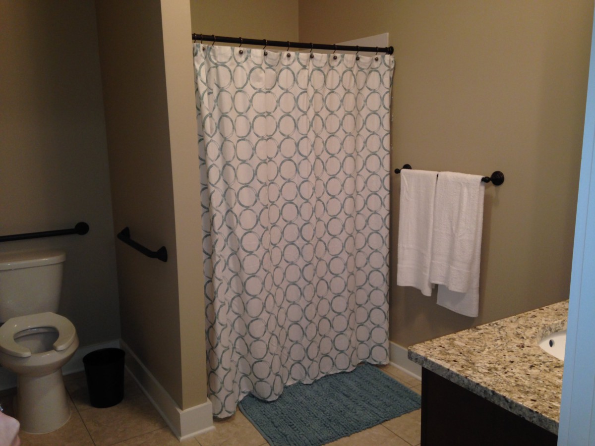 A bathroom featuring a decorative shower curtain, towel rack with a white towel, and a blue bath mat on the floor.
