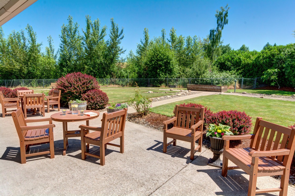 A serene backyard patio with wooden furniture surrounded by lush greenery.