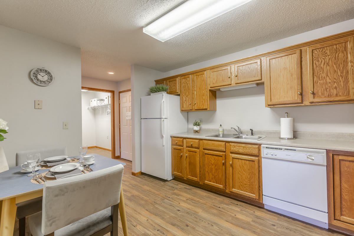 A cozy apartment kitchen with wooden cabinetry, a refrigerator, and a small dining area.