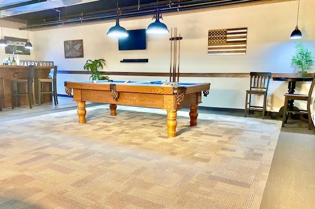 A game room featuring a wooden pool table under hanging lights, with a minimalistic decor.
