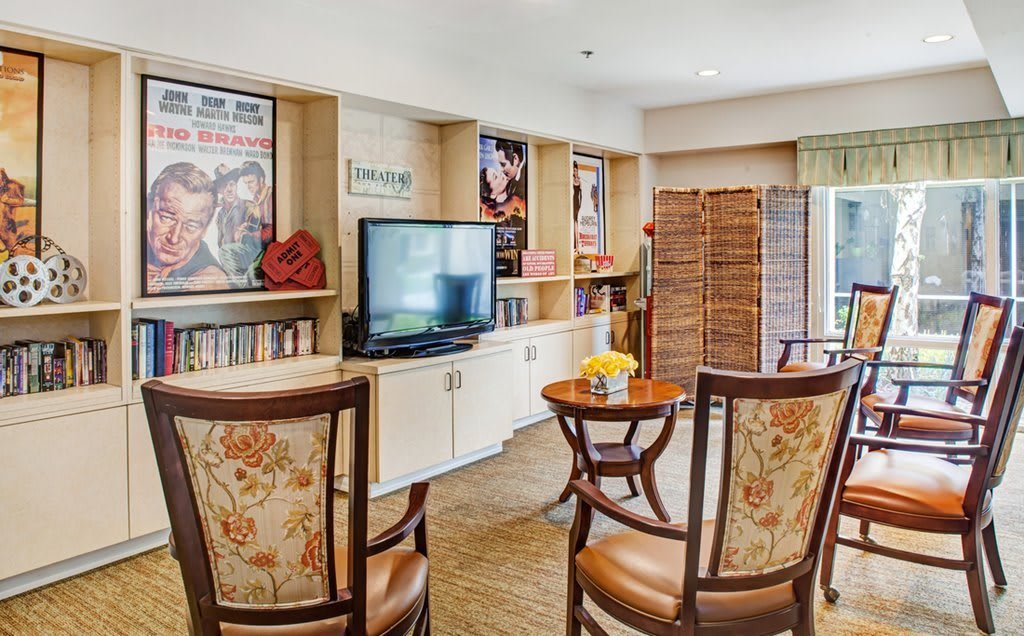 A cozy living room with classic wooden chairs, a television, and shelves adorned with posters.