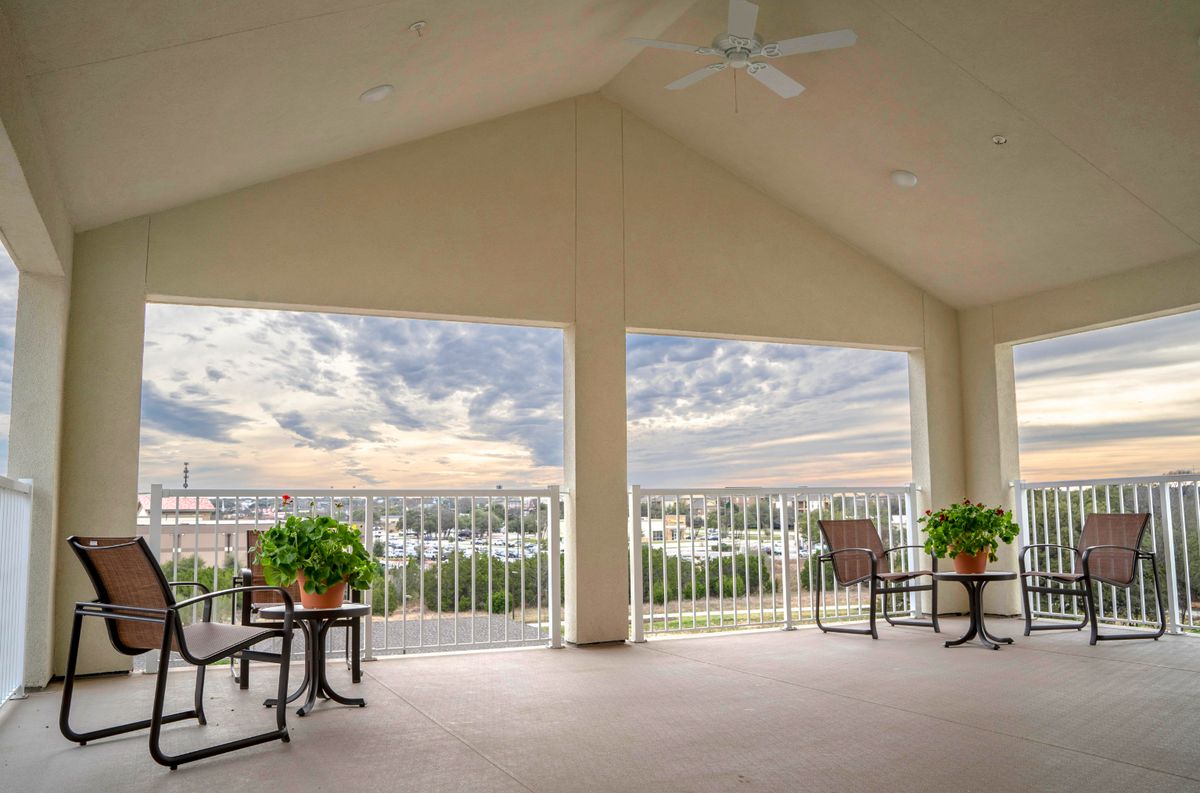 A spacious covered patio with seating and potted plants, offering a scenic view of the skyline.