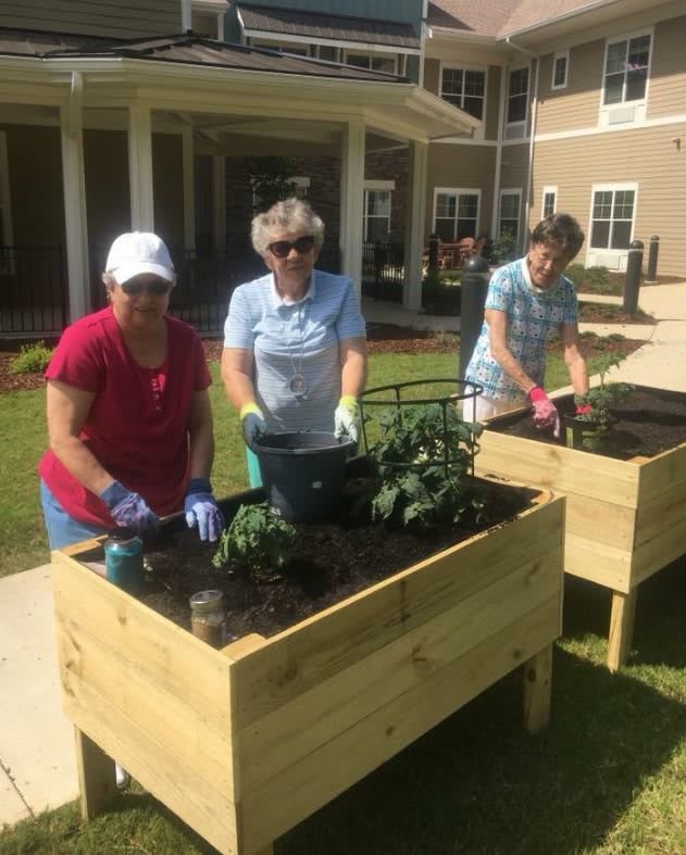 A group of people tending to plants in raised garden beds outside a building.