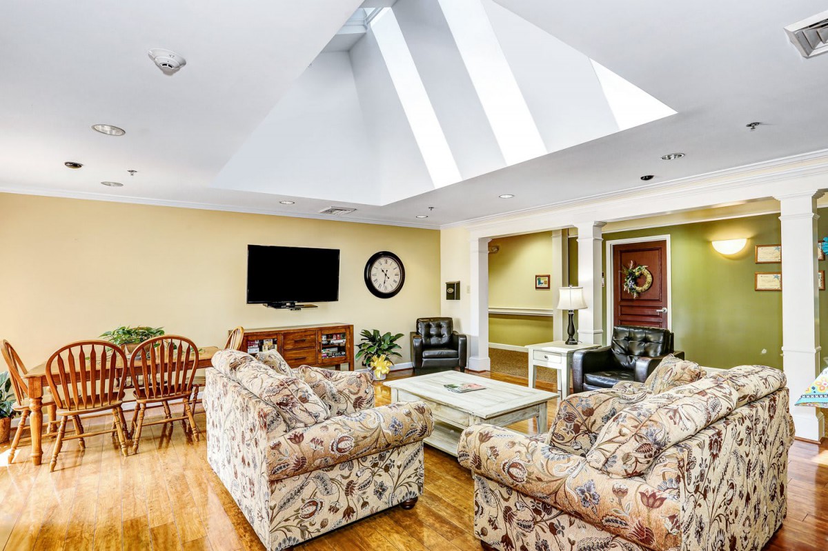 A cozy living room with a skylight, floral sofas, a television, and wooden flooring.