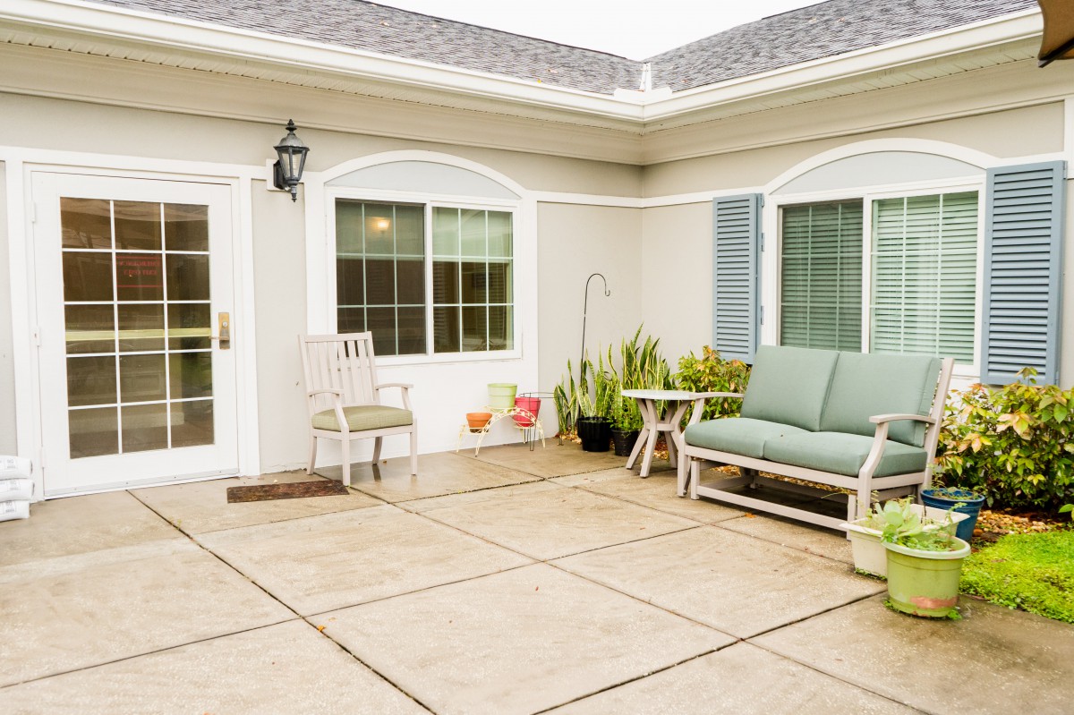 A cozy patio with outdoor seating, potted plants, and large windows.