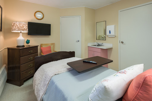 A cozy and well-equipped hospital room with two beds, a television, and a sink area.