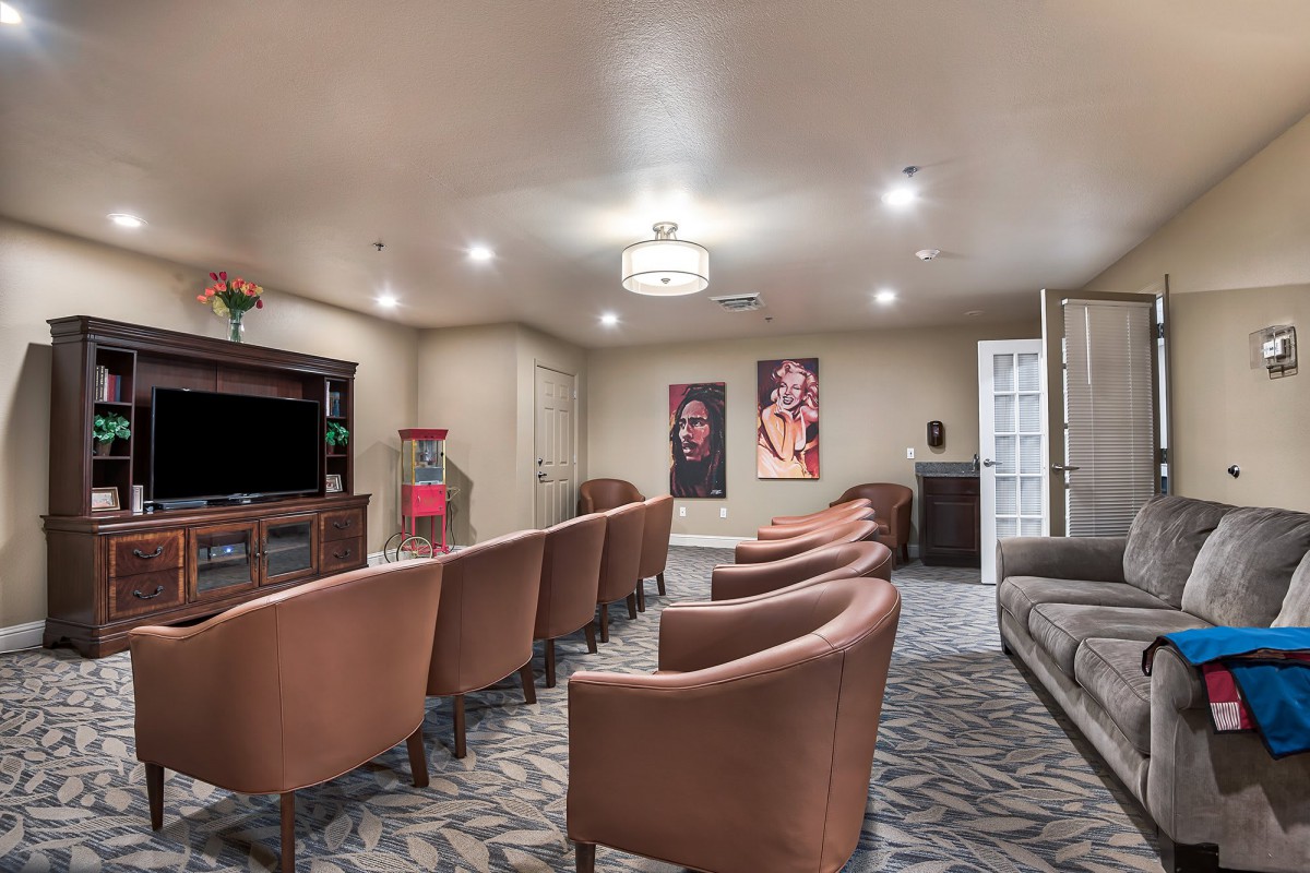 A cozy room with rows of chairs facing a television, complemented by a patterned carpet and artwork on the walls.