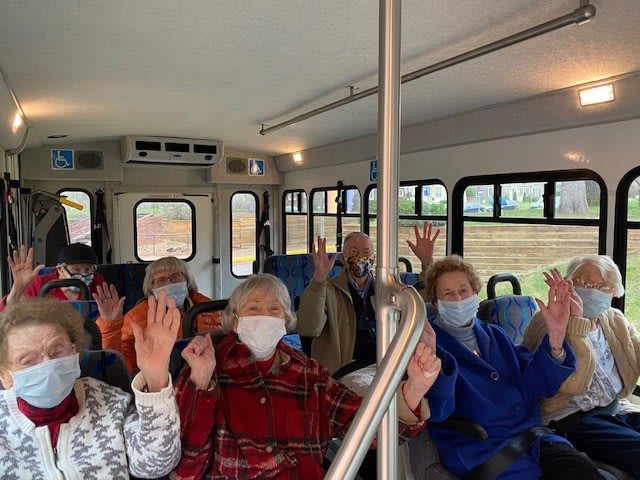 A group of elderly individuals wearing masks and raising their hands while seated inside a bus.