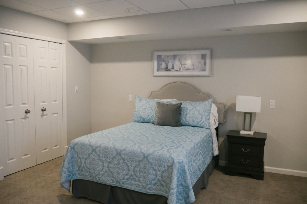 A cozy bedroom with a neatly made bed, featuring blue patterned bedding and a nightstand with a lamp.