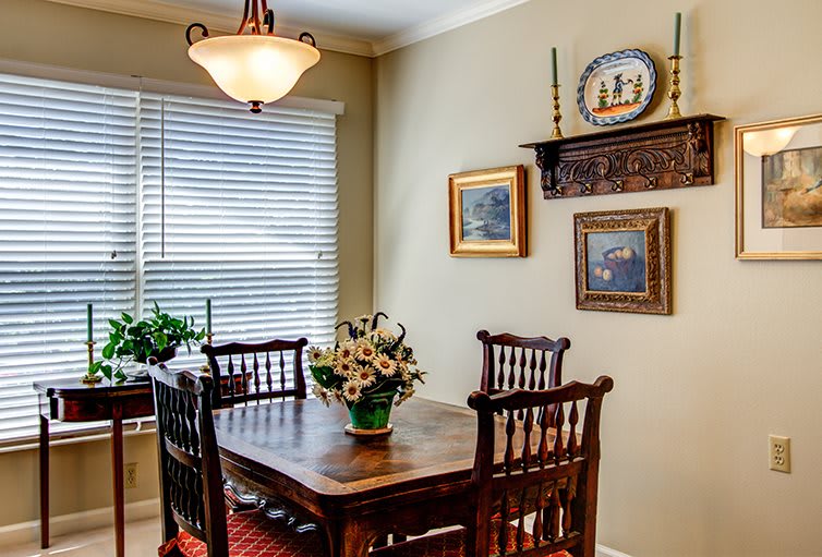 A cozy dining room with a wooden table set, decorated with flowers and paintings.