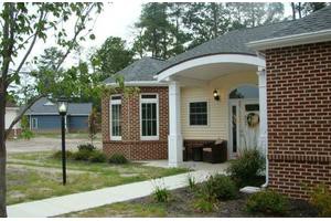 A small residential building with a brick facade, surrounded by a garden and pathway.