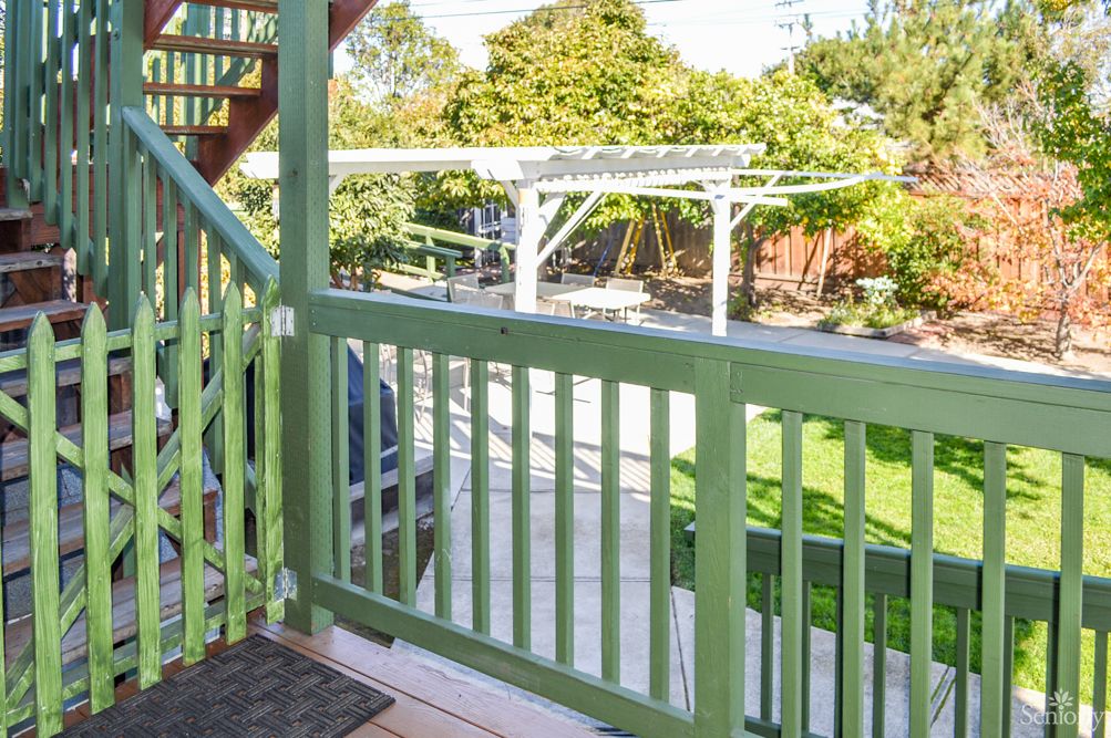 A view from a porch overlooking a green backyard with a wooden fence and garden.