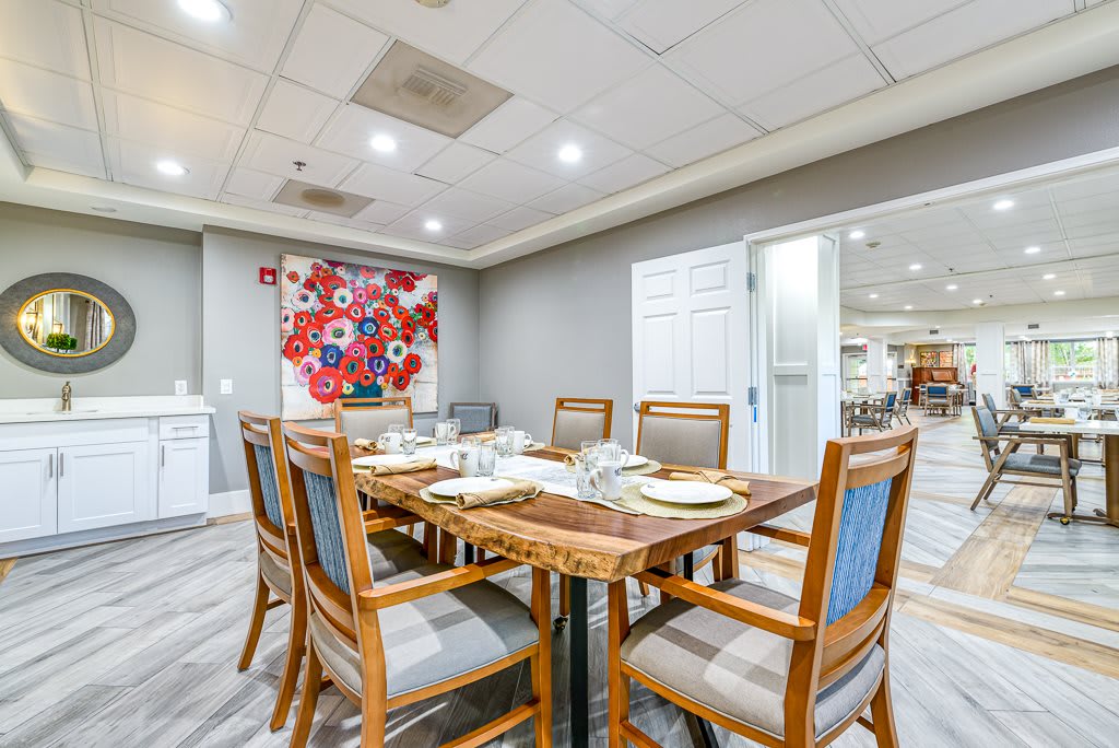 A modern dining room with a wooden table and six chairs, featuring colorful artwork on the wall.