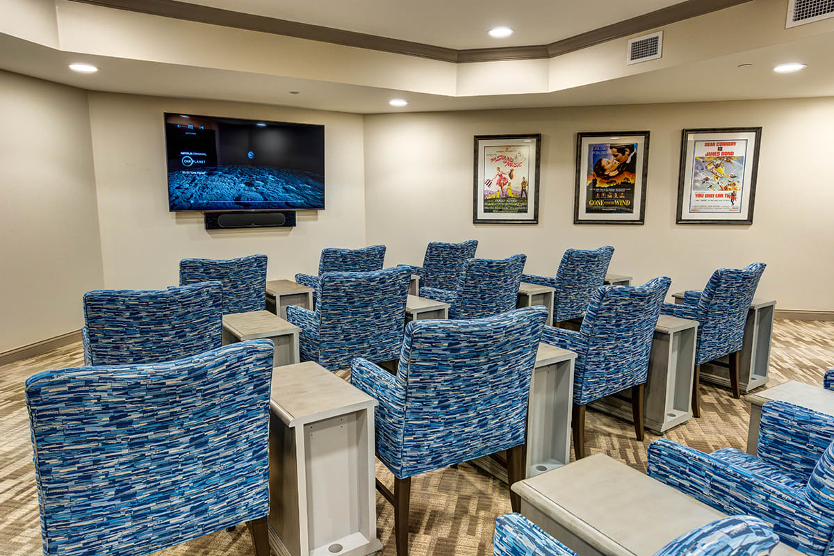 A small theater room with blue upholstered chairs facing a large television screen, surrounded by framed posters on the walls.