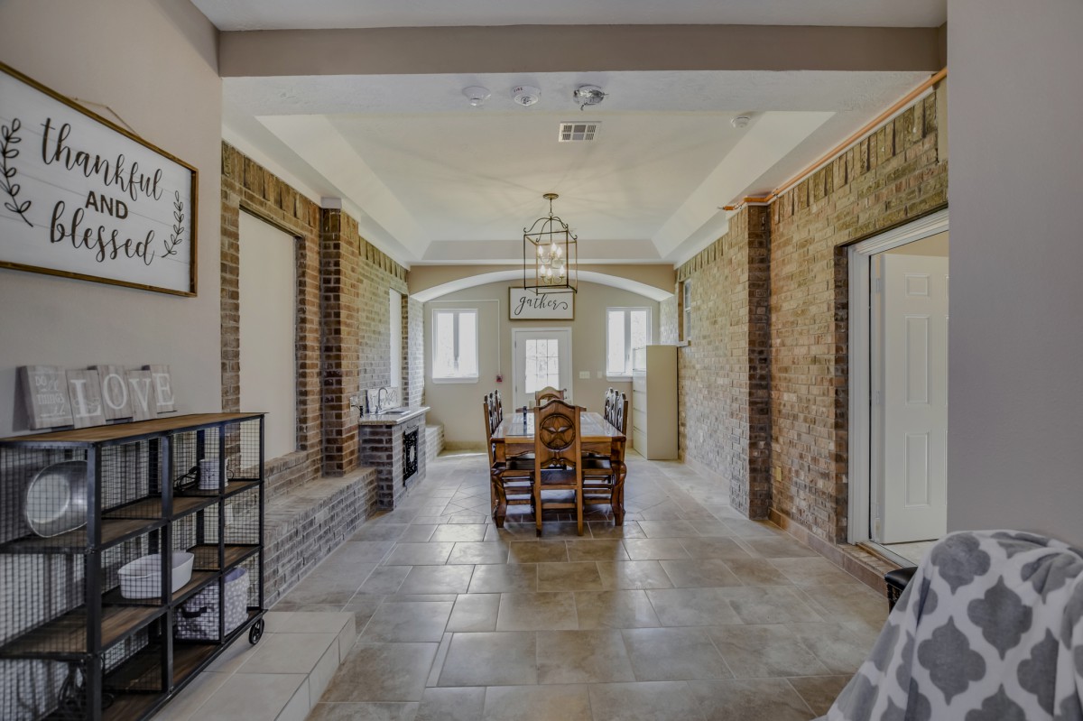 A stylish dining room with exposed brick walls, a central wooden table set under a decorative ceiling light, and large windows allowing natural light to fill the space.