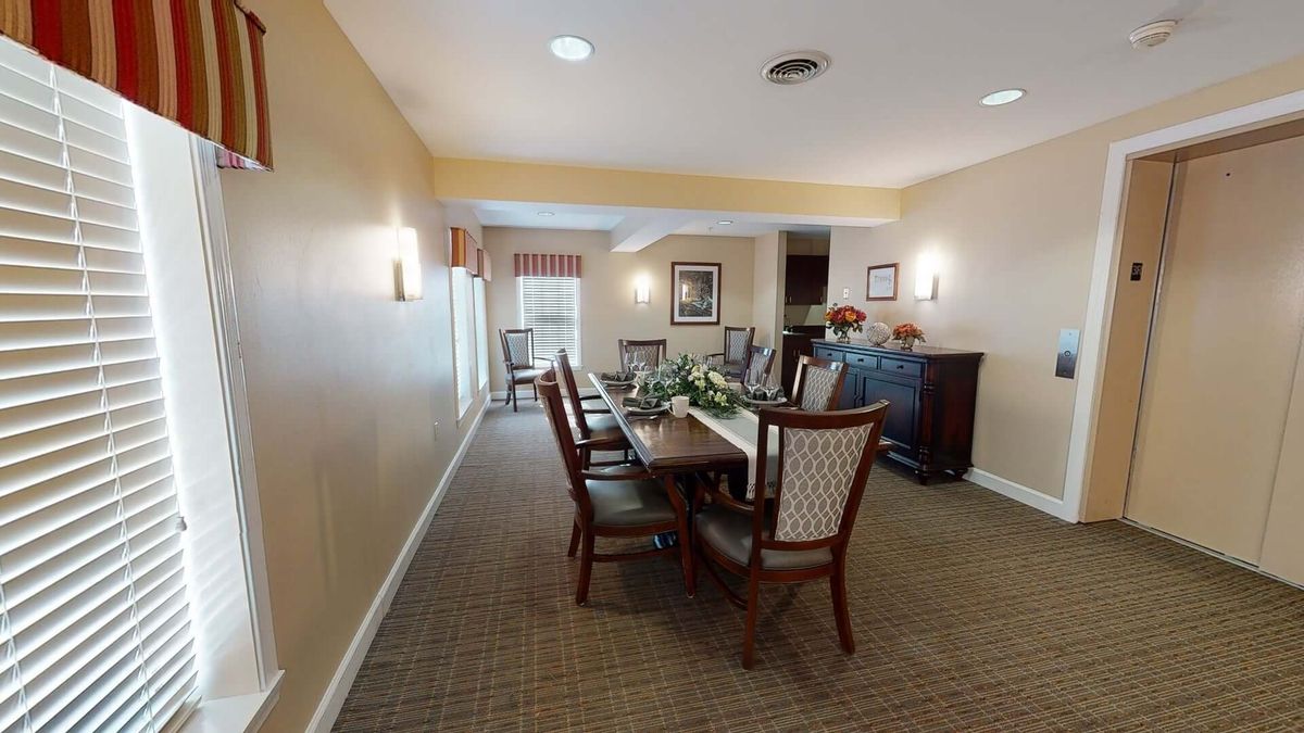 A well-furnished dining room with a long table and chairs, featuring elegant decor and carpeting.