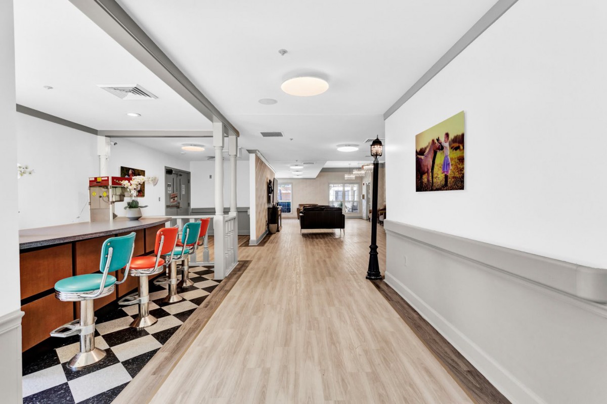 A retro-themed diner interior with colorful seating and a black-and-white checkered floor, leading into a hallway.