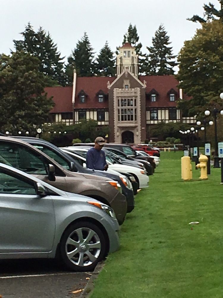 A row of parked cars in front of a historic building surrounded by trees.