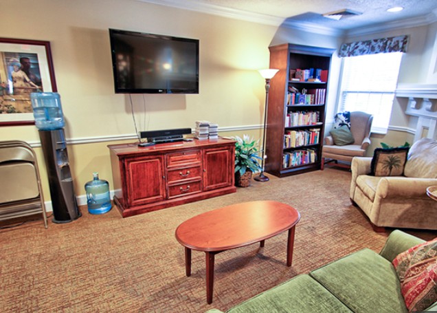 A cozy living room with a mounted TV, bookshelf, and comfortable seating.