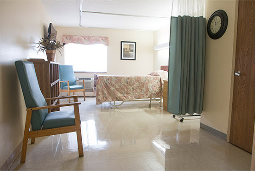 A quiet hospital patient room featuring a bed, armchair, and privacy curtain.