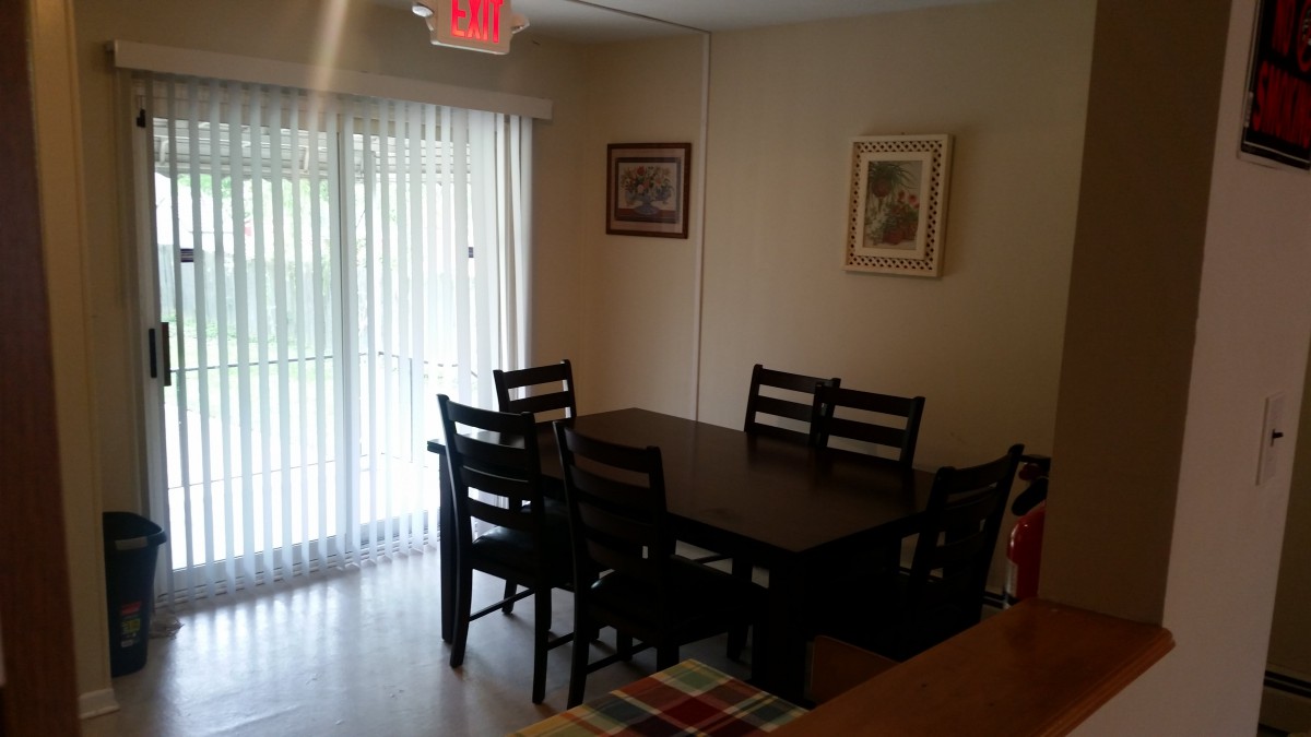A cozy dining room with a dark wooden table and chairs, complemented by framed artwork and natural light from a sliding glass door.