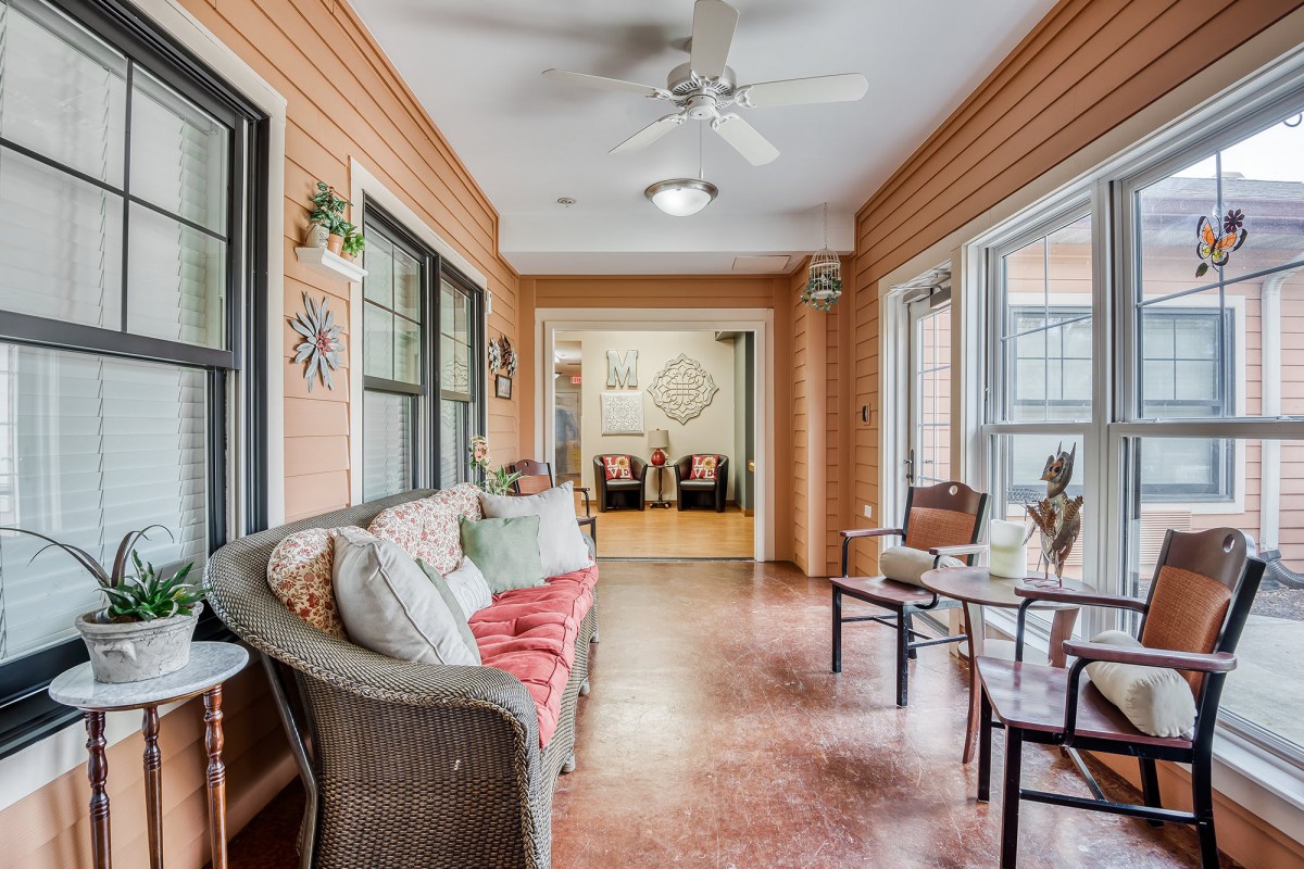A cozy sunroom featuring wicker furniture, large windows, and a ceiling fan.