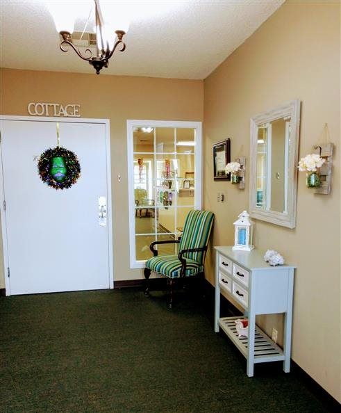 A welcoming entryway with a decorated door, a chair, and a small table with a mirror and lamp.