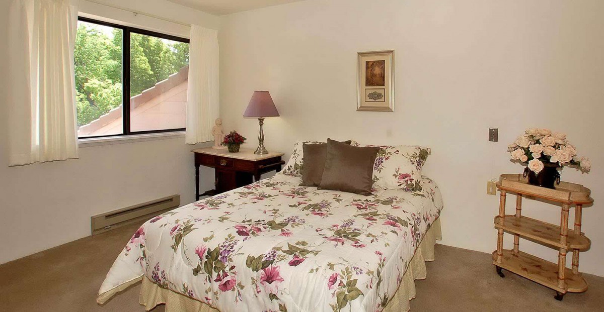A cozy bedroom with floral bedding and soft lighting, featuring a small window and decorative elements.