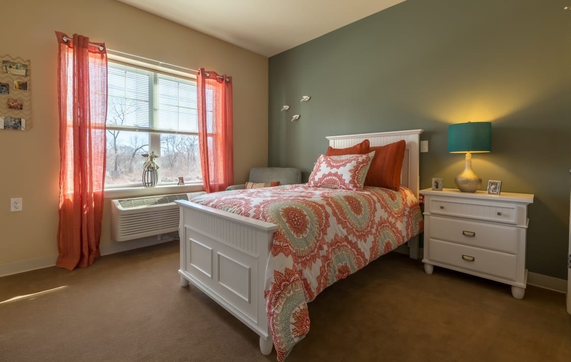 A cozy bedroom with a neatly made bed, colorful bedding, and a window with curtains.