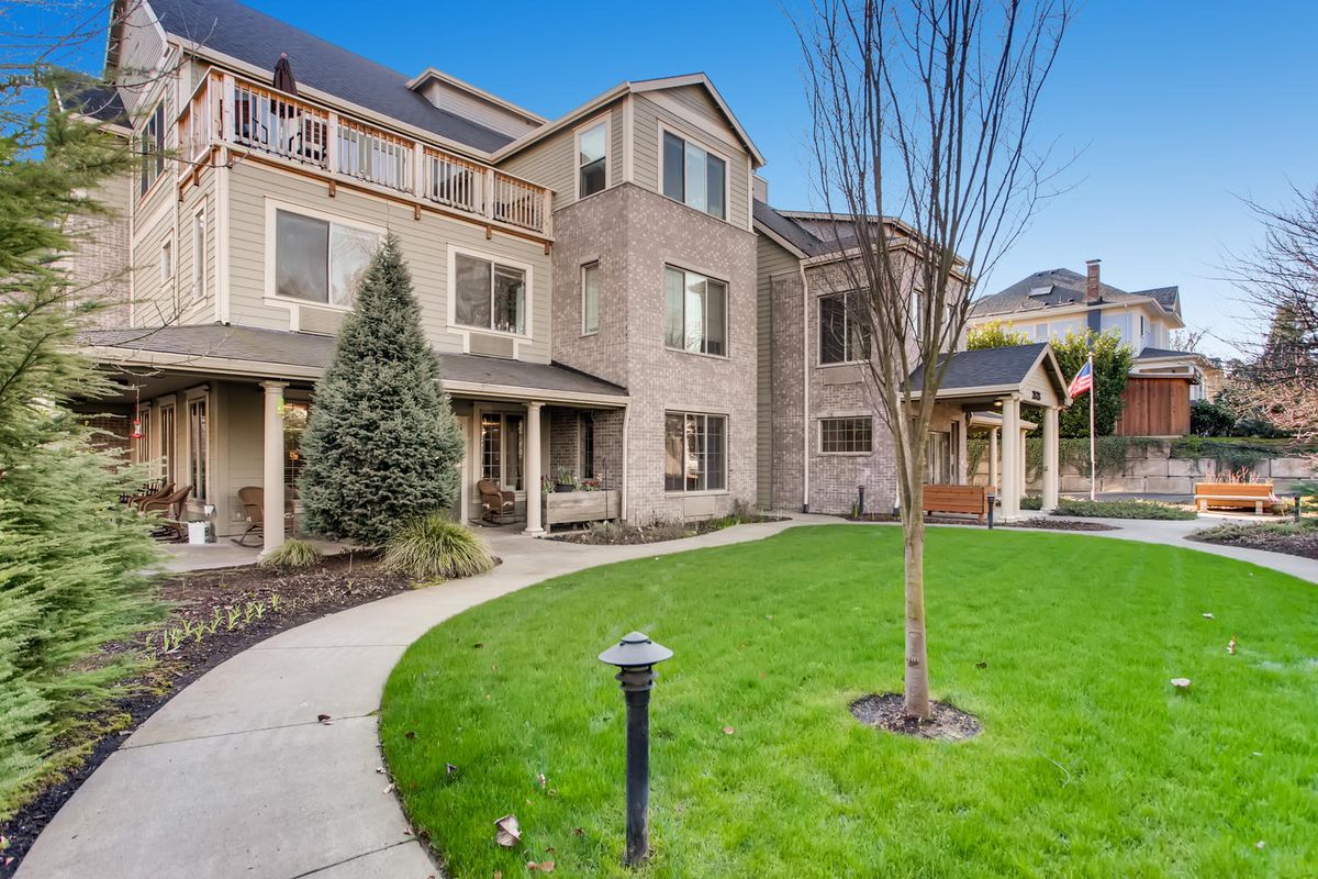 A well-maintained residential building with a manicured lawn and surrounding trees.