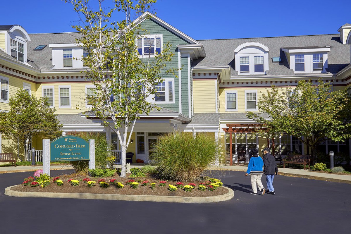 A residential building with a landscaped entrance on a sunny day, where two people are walking.
