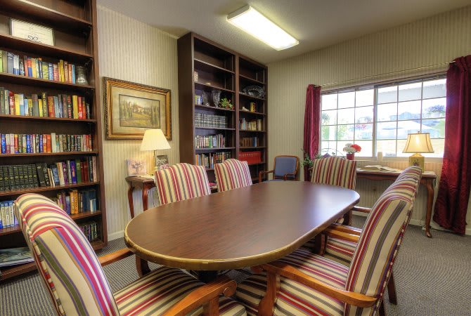 A cozy conference room with a wooden meeting table, striped chairs, and bookshelves by the window.