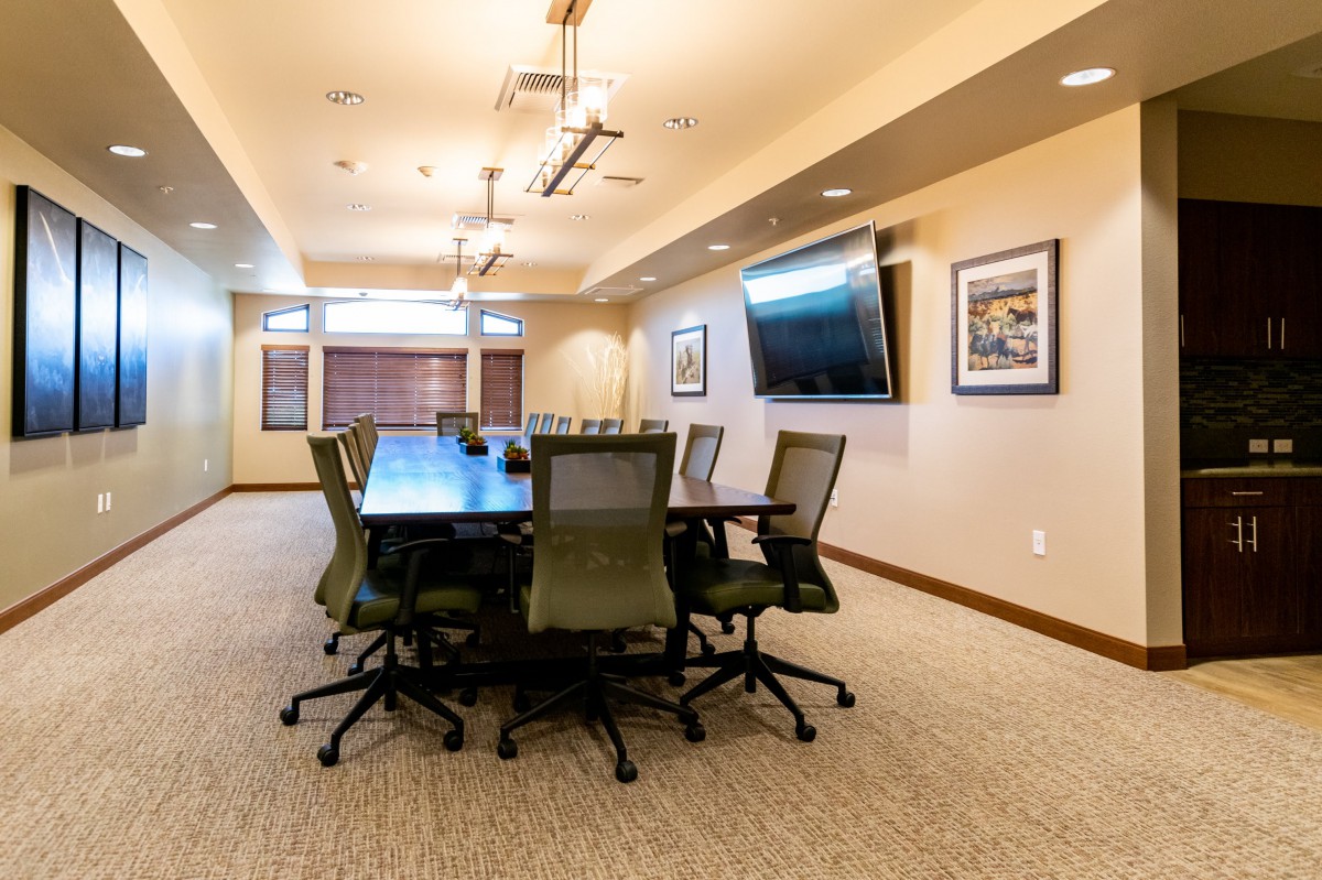 A well-lit conference room with a large table, chairs, and a wall-mounted television.
