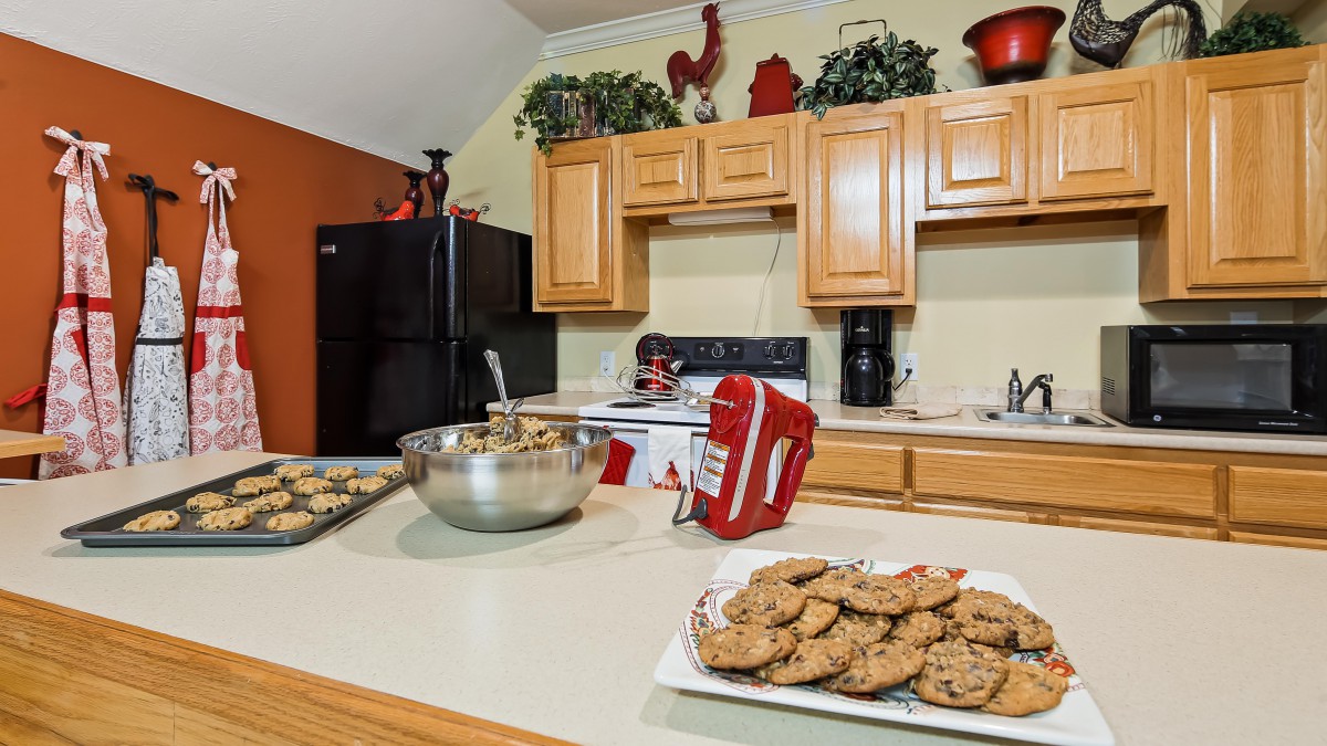 A kitchen scene featuring freshly baked cookies on a countertop, with a mixer and baking ingredients in the background.