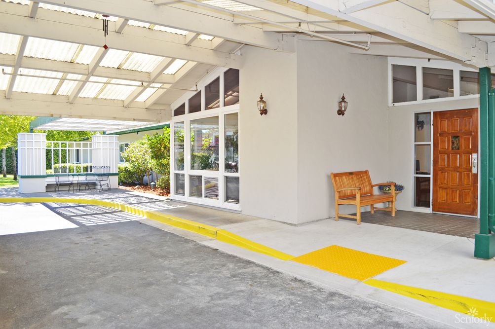 A modern patio next to a driveway with a wooden bench and glass windows.