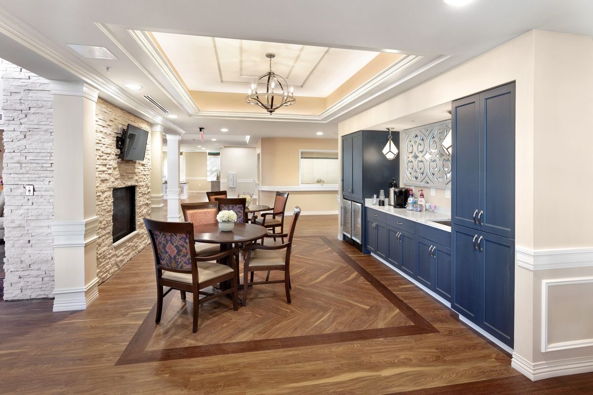 A modern and elegant living room with a dining area, featuring wood flooring, a chandelier, and stylish cabinetry.