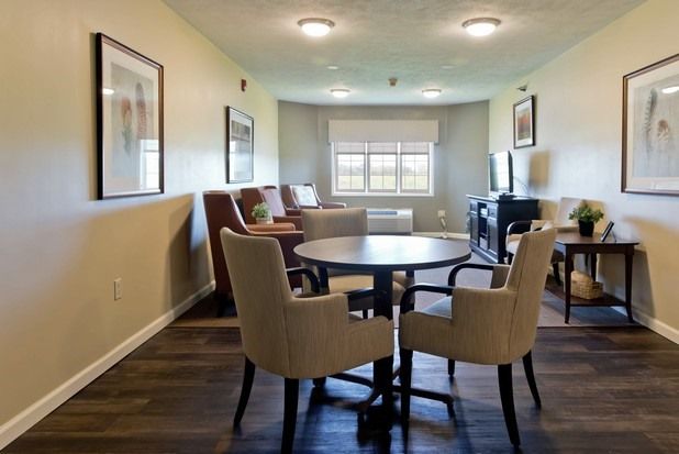A cozy living room with a round table and chairs, featuring ample natural light from a large window.