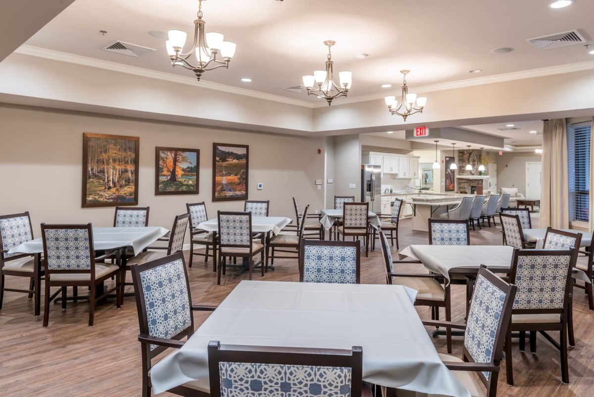 An elegant dining area with neatly arranged tables and chairs, illuminated by chandeliers.