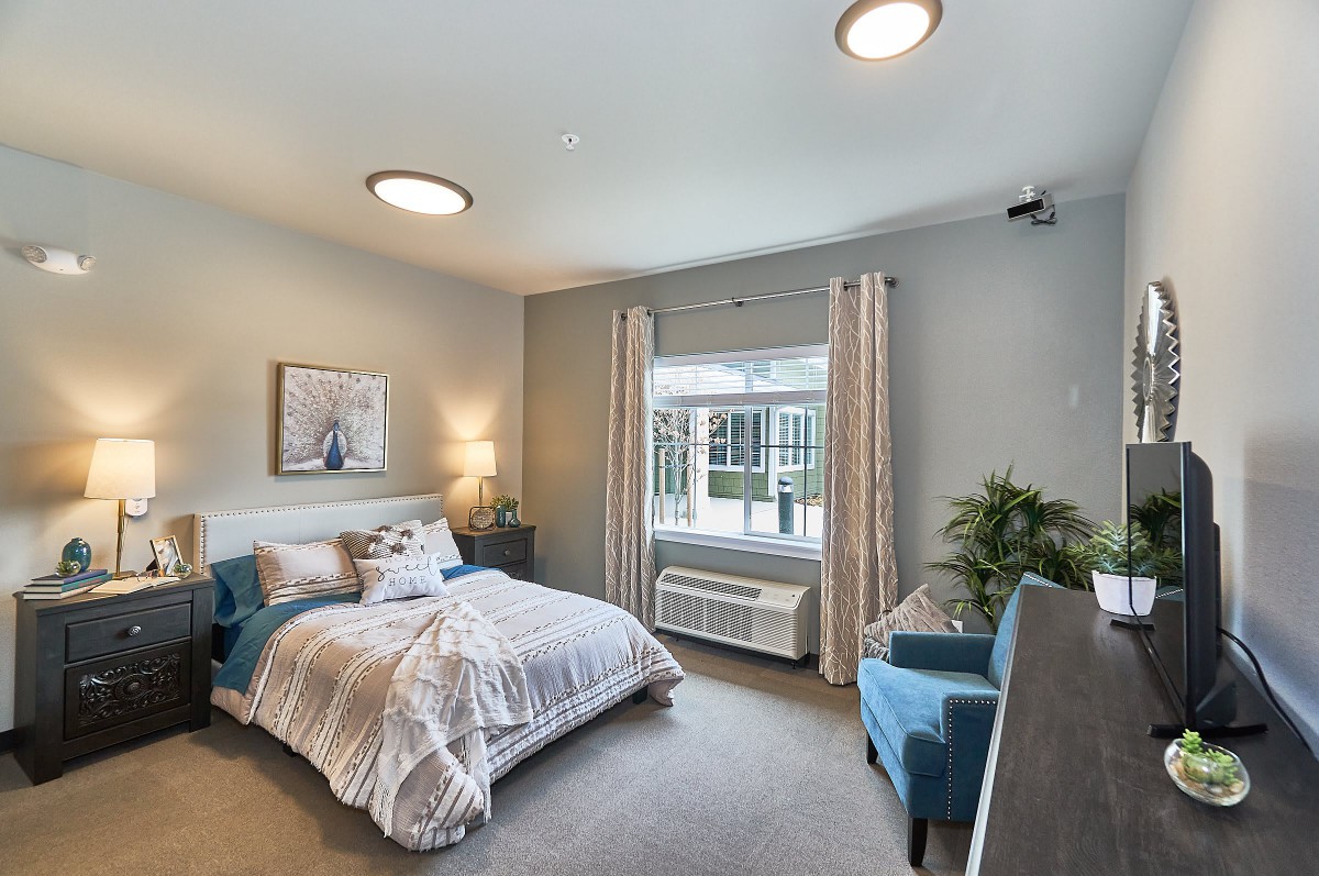A cozy and modern bedroom with a neatly made bed, armchair, and large window letting in natural light.